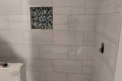 Contemporary bathroom wall featuring large white tiles and a mosaic accent for stylish decor.