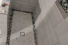 Close-up of a bathroom shower with large wall tiles and a decorative mosaic border on the floor.