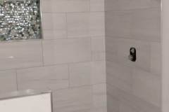 Elegant bathroom shower featuring white tiles and a decorative mosaic accent wall.
