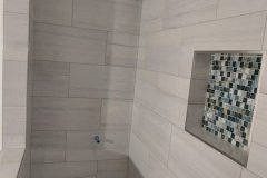 Elegant white tiled shower featuring a mosaic accent wall, showcasing high-quality tile work by Grapme Tile Works Corp.