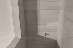 Elegant shower area featuring white ceramic tiles and a mosaic tile floor, showcasing quality craftsmanship by Grapme Tile Works Corp.