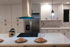 A contemporary kitchen showcasing a stylish tile backsplash, white cabinetry, and a spacious island with seating.