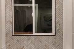 Elegant herringbone tile wall with window, perfect for contemporary interior design. Expert tile installation by GRAPME TILE WORKS CORP.