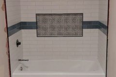 Modern bathroom with white subway tiles, mosaic inset, and patterned floor tiles.