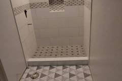 A stylish bathroom shower with white tiles, mosaic accents, and patterned floor tiles, showcasing quality tile work.