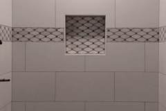 Interior bathroom wall featuring white tiles and mosaic border detail.