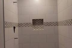 Elegant shower area featuring white tiles, a decorative border, and built-in niche for toiletries.