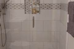 Elegant bathroom shower featuring white tiles, decorative border, and glass door for a sleek look.
