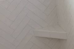 Elegant white herringbone tile wall with a built-in shelf, showcasing high-quality tile installation by Grapme Tile Works.