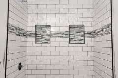 This image showcases a bathroom wall featuring classic white subway tiles, accented with a decorative mosaic border and two built-in niches for storag.