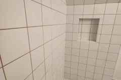 Modern bathroom wall with white ceramic tiles and recessed niche detail.