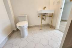 Clean, contemporary bathroom featuring hexagon tile flooring, a white toilet, and a stylish sink with gold fixtures.