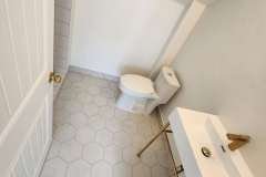 Contemporary bathroom featuring hexagon tiles, a sleek toilet, and stylish sink with gold accents.
