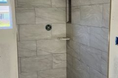 A contemporary gray tile shower featuring a pebble stone floor and minimalist design, perfect for modern bathrooms.