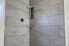 A sleek, modern gray tile shower featuring a pebble stone floor and a built-in niche for toiletries.