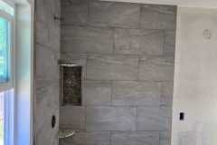 Contemporary bathroom shower with gray tiles and pebble floor, showcasing expert tiling craftsmanship.