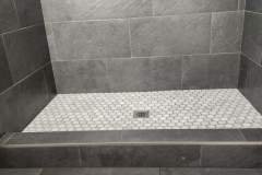 Contemporary gray tiled shower with hexagon floor tiles, showcasing durable and stylish bathroom design.