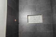 A contemporary black tiled shower featuring a recessed niche and white hexagon floor tiles, showcasing stylish bathroom design.