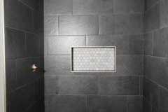Contemporary black tiled shower featuring a white mosaic floor and a recessed niche for toiletries.