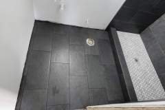 A sleek black tiled shower space featuring textured floor tiles, showcasing quality craftsmanship by Grapme Tile Works.