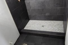 Contemporary black tiled shower featuring a built-in niche and white mosaic floor tiles, ideal for stylish bathroom renovations.