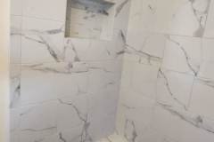 Elegant marble shower with niche and pebble floor, highlighting expert tile craftsmanship by Grapme Tile Works.