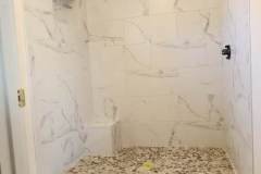 Newly installed marble shower with pebble floor, showcasing high-quality tile work by Grapme Tile Works Corp.