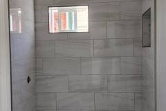 Stylish bathroom shower with large marble-effect tiles and a small window for natural light.