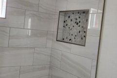 A sleek, modern shower wall featuring large marble-like tiles, a recessed niche, and a pebble stone floor for a stylish bathroom upgrade.