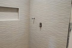 Up of a contemporary bathroom shower with textured white tiles, built-in niche, and pebble floor.
