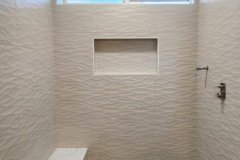 A contemporary shower area with textured wall tiles, a small bench, and a built-in niche for toiletries.