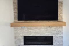Elegant living room featuring a sleek fireplace below a mounted flat-screen TV on a textured stone wall.