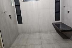 A clean, modern bathroom featuring light-colored tiles, black accents, and a frosted window for natural light.
