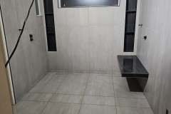 A sleek, modern bathroom featuring large gray tiles, a built-in shower, and a small bench for comfort and convenience.