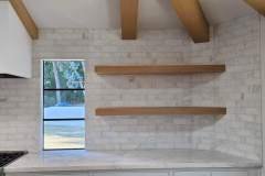 Contemporary kitchen interior featuring white brick walls, wooden shelves, and natural light from a large window.
