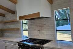 A bright, contemporary kitchen featuring a tile backsplash, white cabinets, and wooden shelves, highlighting quality tile work by Grapme Tile Works Co.