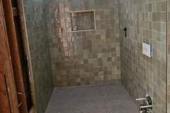 Bathroom shower with mosaic tiles, natural light, and built-in niche for toiletries.