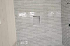 A sleek, modern shower space featuring gray subway tiles, a built-in niche, and a tiled bench for comfort and style.
