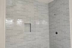 Contemporary bathroom shower featuring gray subway tiles, a recessed niche, and ongoing ceiling fixture setup.