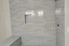 Interior view of a contemporary shower featuring gray subway tiles, a built-in niche, and a tiled bench for comfort and style.