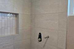 Close-up of a contemporary shower wall featuring beige tiles and pebble flooring, showcasing quality tile work by Grapme Tile Works Corp.