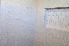 A clean, modern shower space featuring large wall tiles, a pebble stone floor, and a recessed niche for convenience.