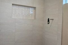 Bathroom shower featuring beige tiles, pebble floor, and a recessed niche for storage.