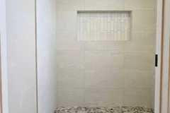 Elegant bathroom shower with beige tiles and mosaic detail, showcasing quality tile work by GRAPME TILE WORKS CORP.