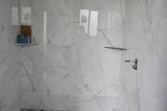 A sleek bathroom shower featuring large marble tiles on the walls and a pebble stone floor for a luxurious look.
