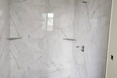 Interior view of a bathroom with marble wall tiles and a mosaic tile floor, showcasing high-quality tile work by Grapme Tile Works Corp.