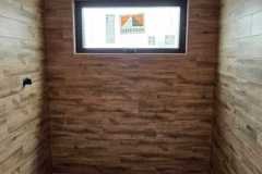 Interior of a bathroom with wood-textured wall tiles and a window, showcasing professional tiling work.