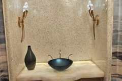 Stylish bathroom vanity featuring beige tiled arch, black vessel sink, and gold wall sconces by Grapme Tile Works.