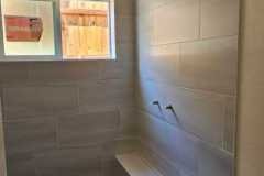 Bathroom shower featuring large tiles, a built-in bench, and a window for ventilation and brightness.