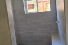 A sleek, modern shower area featuring light-colored tile walls, a small window for natural light, and a built-in bench for comfort.